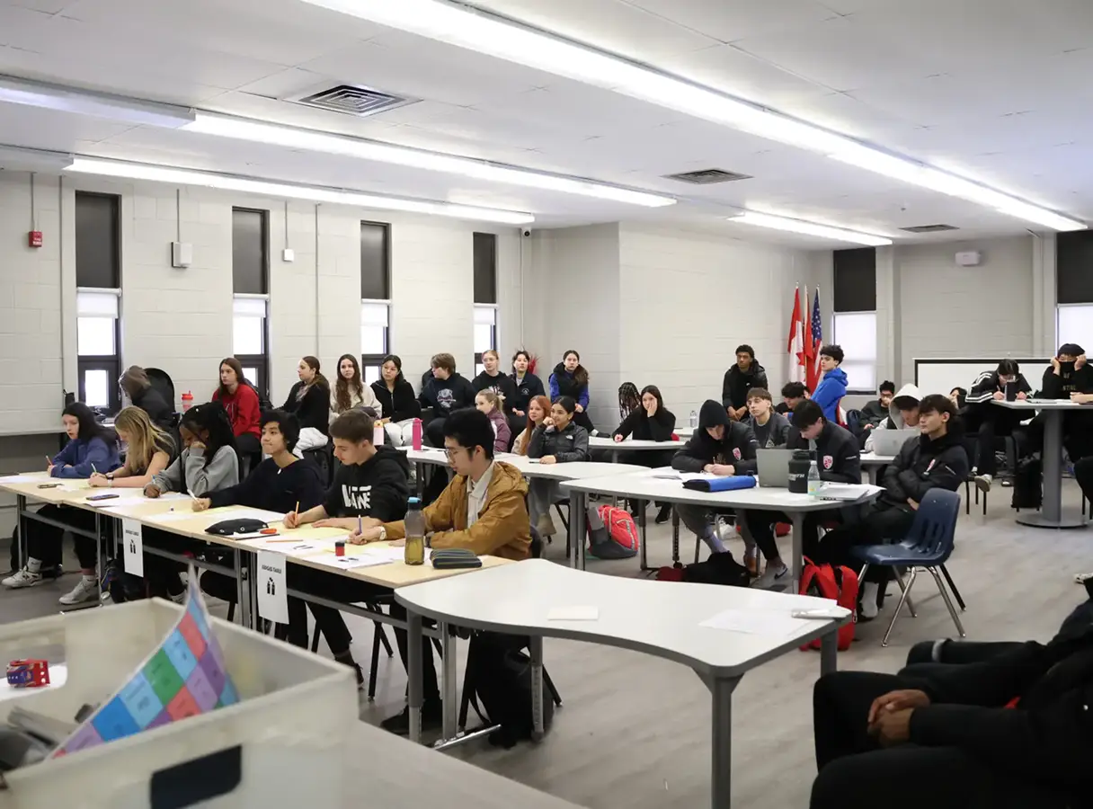 A classroom full of students listens attentively to a lecture, with some taking notes.