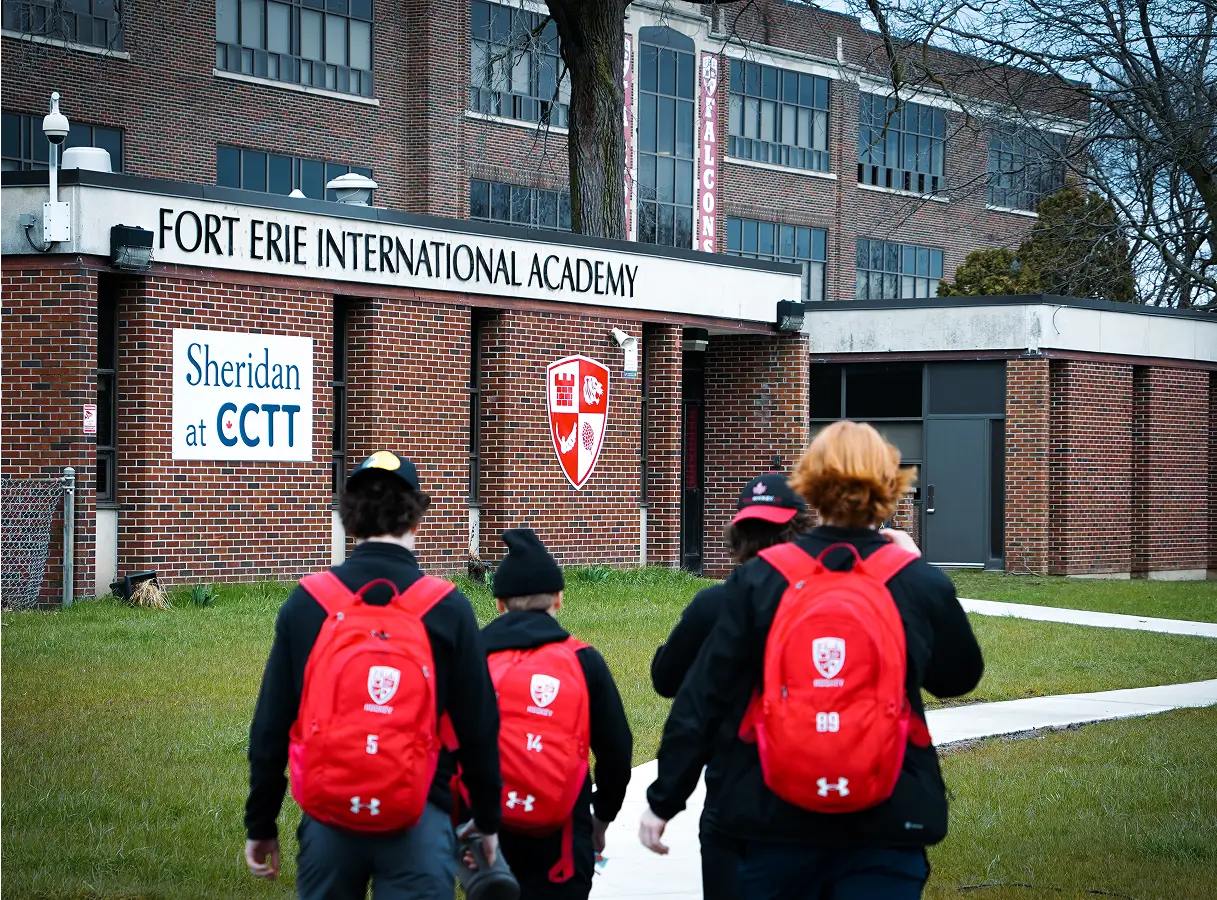 Three students wearing red backpacks walk towards the entrance of Fort Erie International Academy.