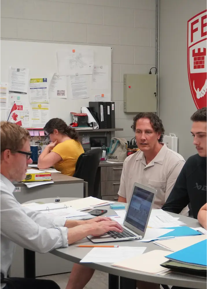Three people sit at a table discussing something on a laptop screen.