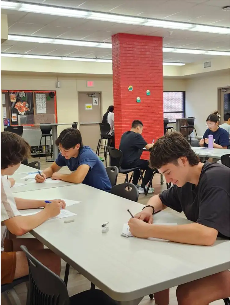Several students sitting at tables in a classroom, writing on papers.
