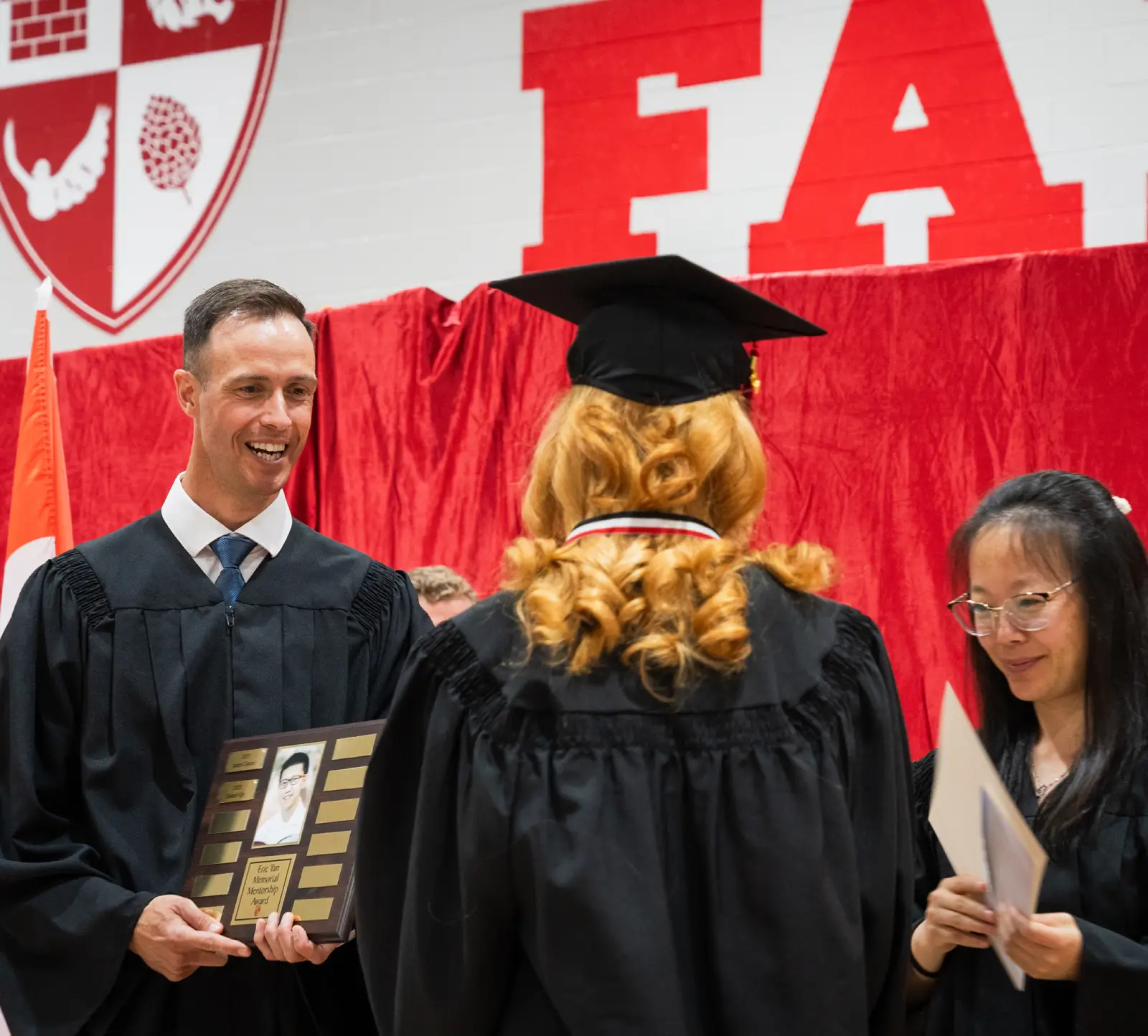 A graduate in cap and gown receives a plaque from a faculty member during a ceremony.