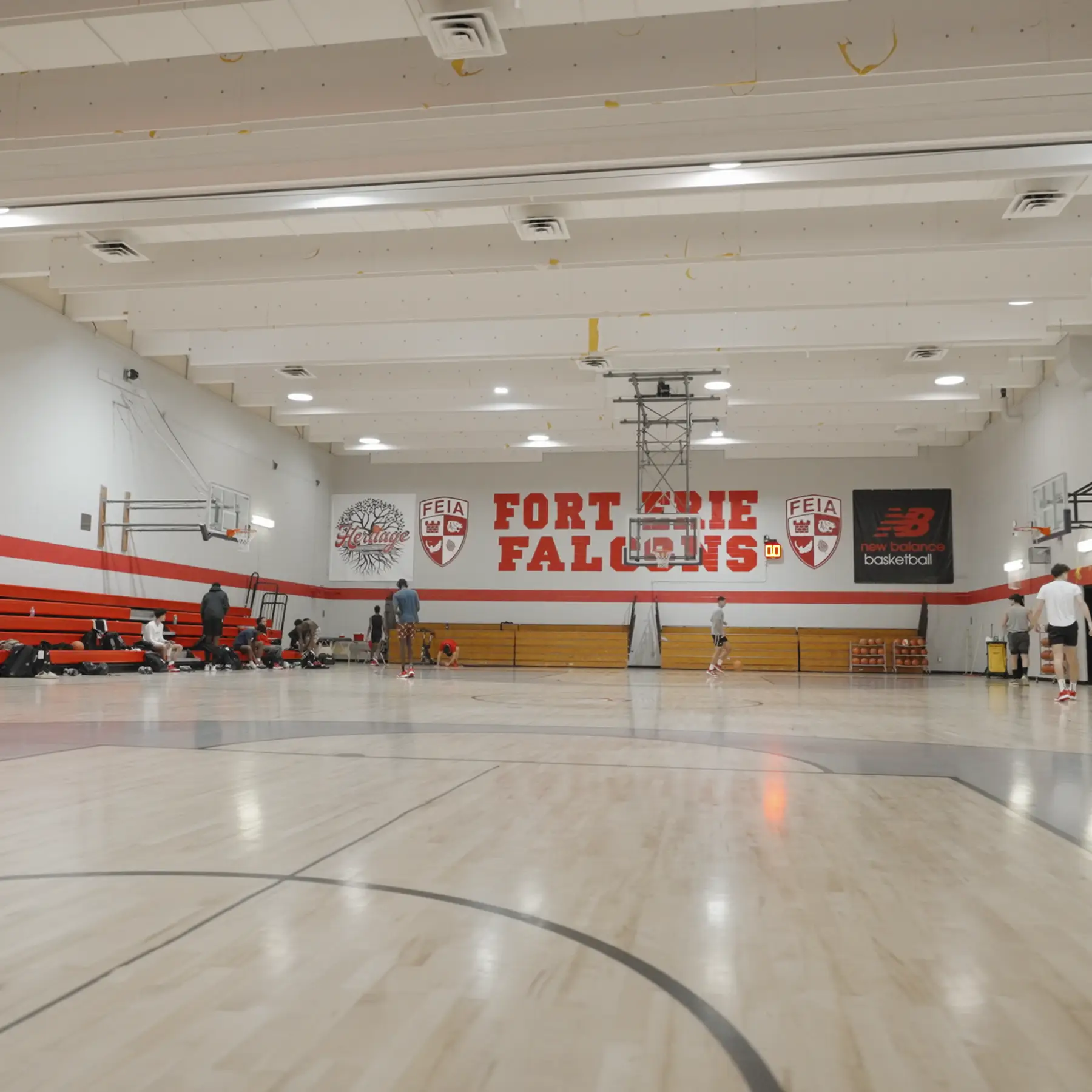 People playing basketball in a gymnasium labeled "Fort Erie Falcons" with red and white walls.