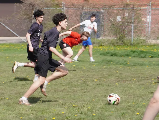 A group of young men playing soccer on a grassy field, chasing the ball.