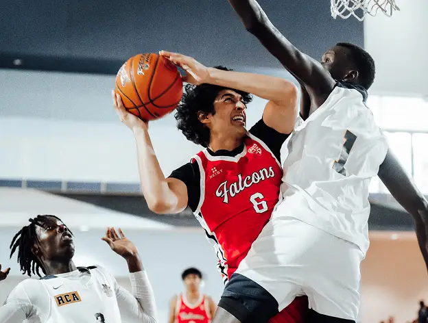 Player in a red jersey attempts a basketball shot, closely defended by opponents in white jerseys.