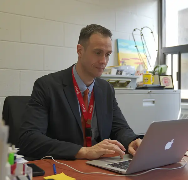 Man in a suit typing on a laptop at a desk in an office.