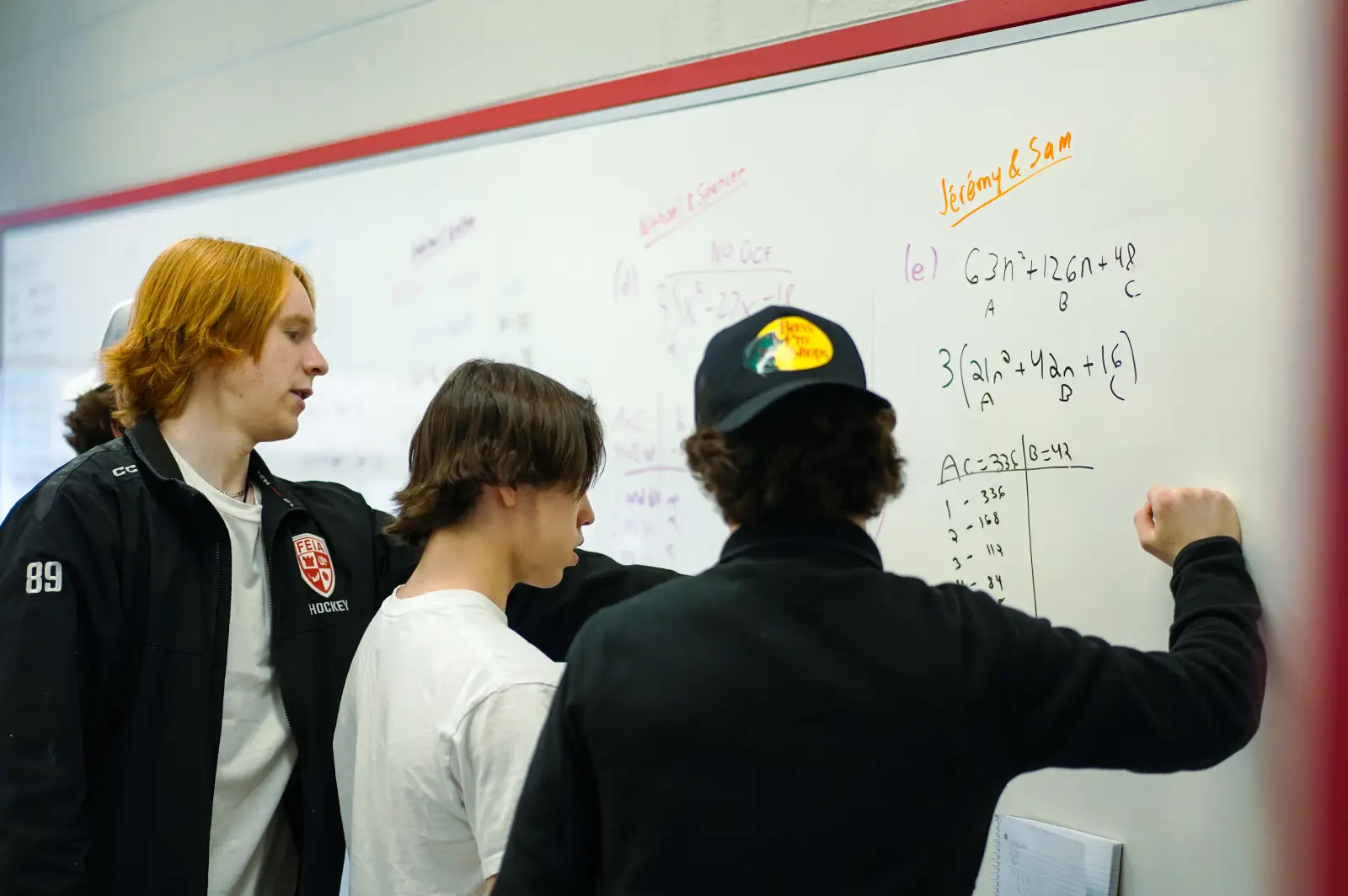 Three people stand at a whiteboard, working on math problems together.