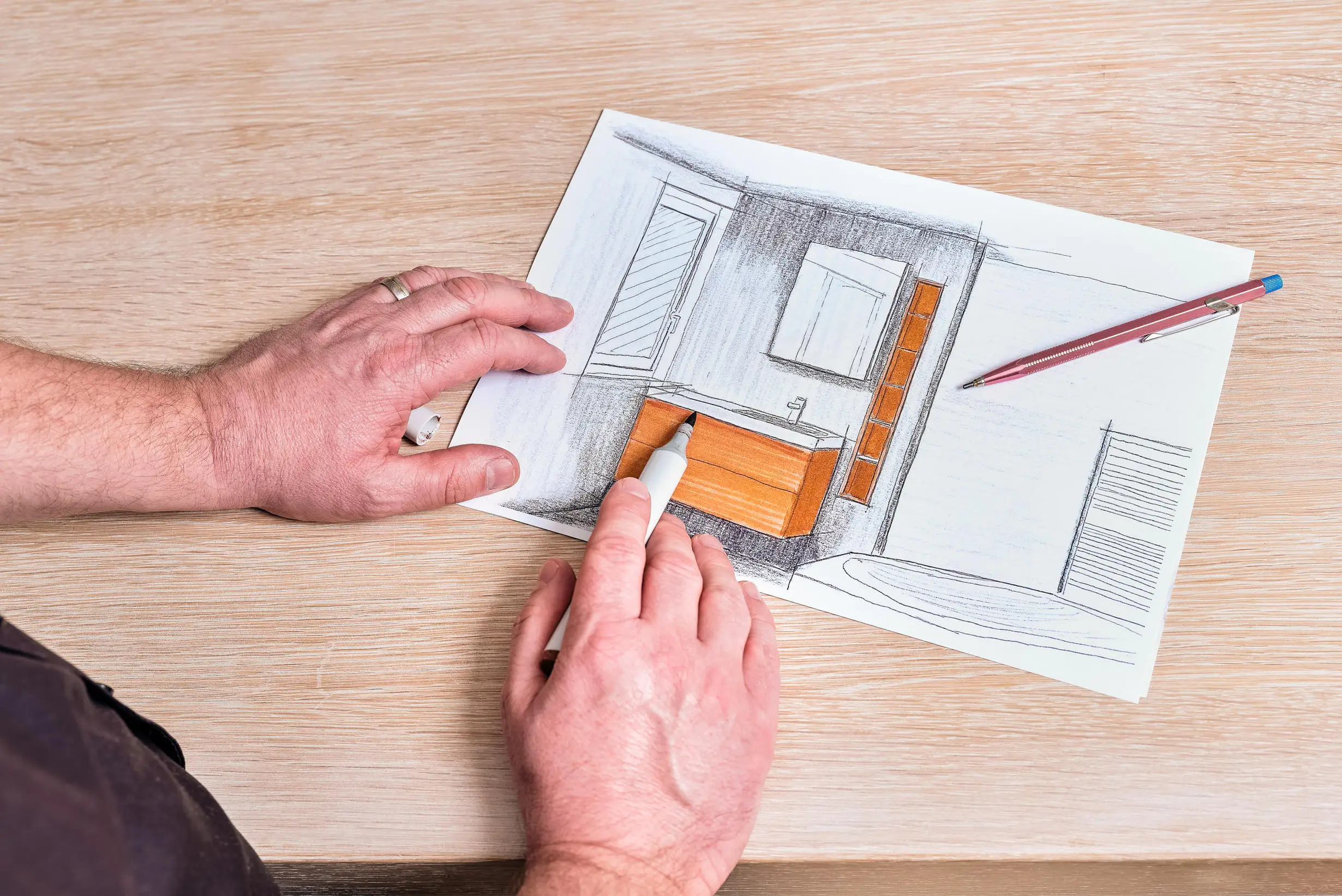 Hände zeichnen mit Marker ein Badezimmerlayout auf Papier mit Holzwaschbeckenunterschrank und Spiegel.