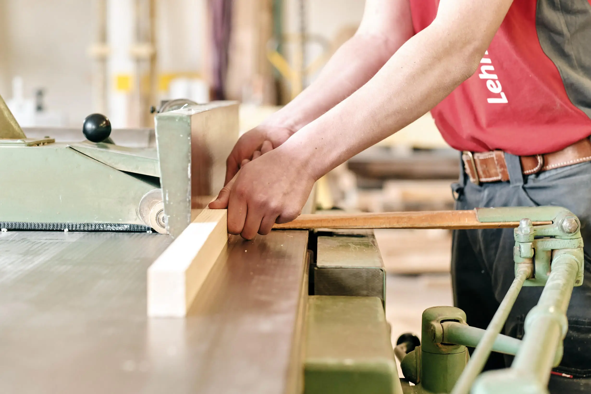 Handwerker arbeitet an einer Holzmaschine und führt ein Brett durch die Führung.