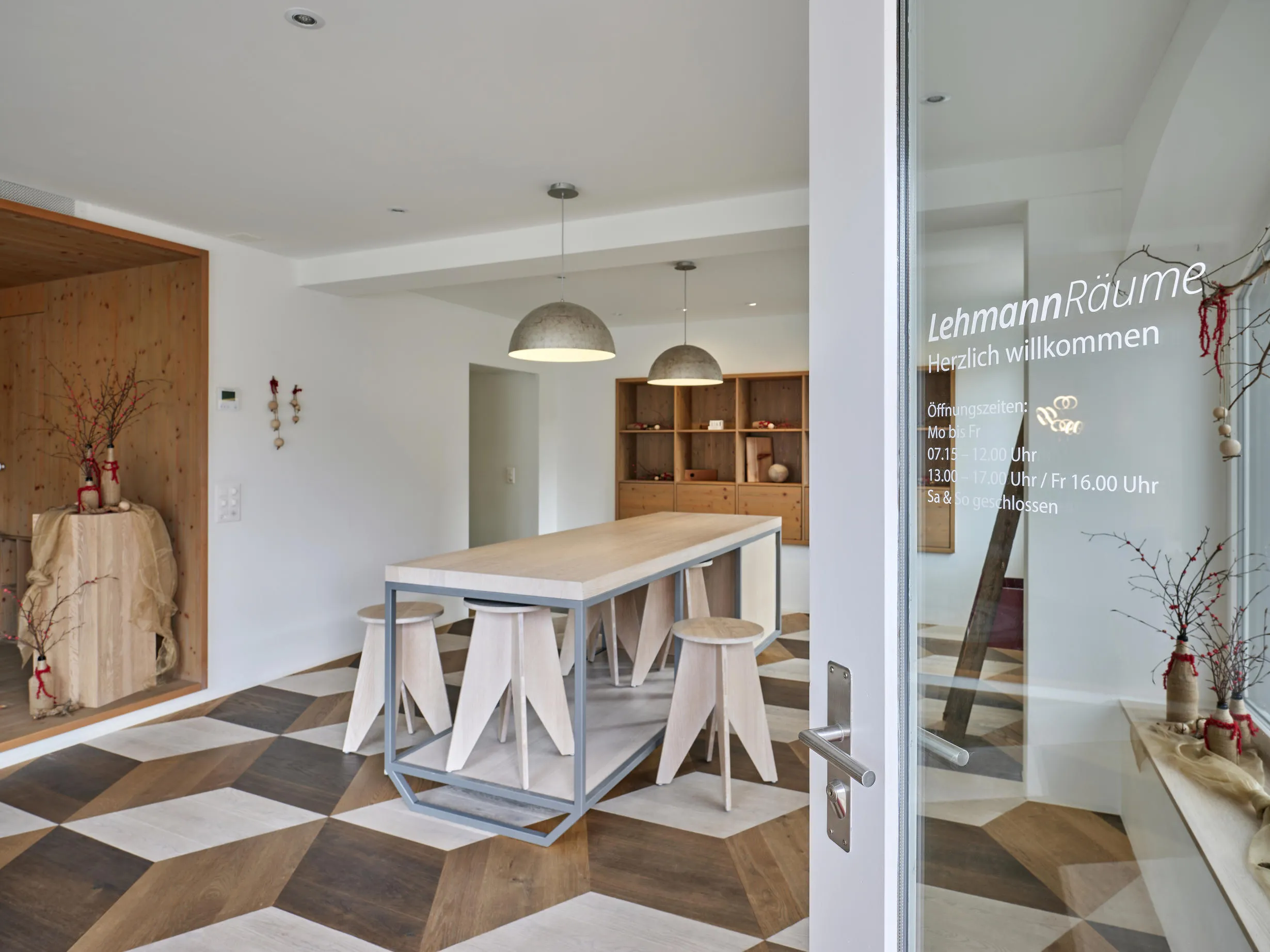 Moderner Raum mit einem langen Tisch mit Holzplatten und Hockern auf einem geometrischen, mehrfarbigen Holzboden.