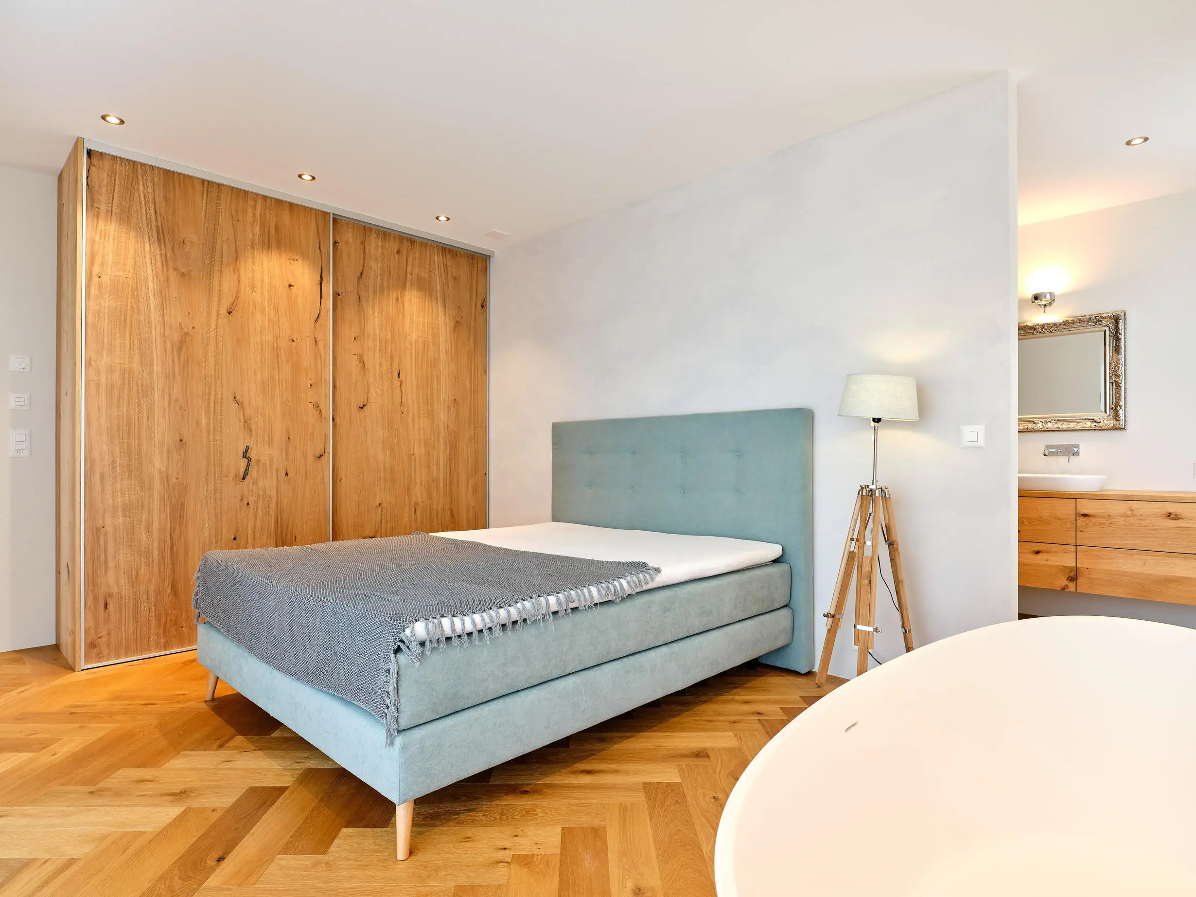 Modernes Schlafzimmer mit hellblauem Polsterbett, grauer Decke, Holzparkettboden und großem Holzkleiderschrank.