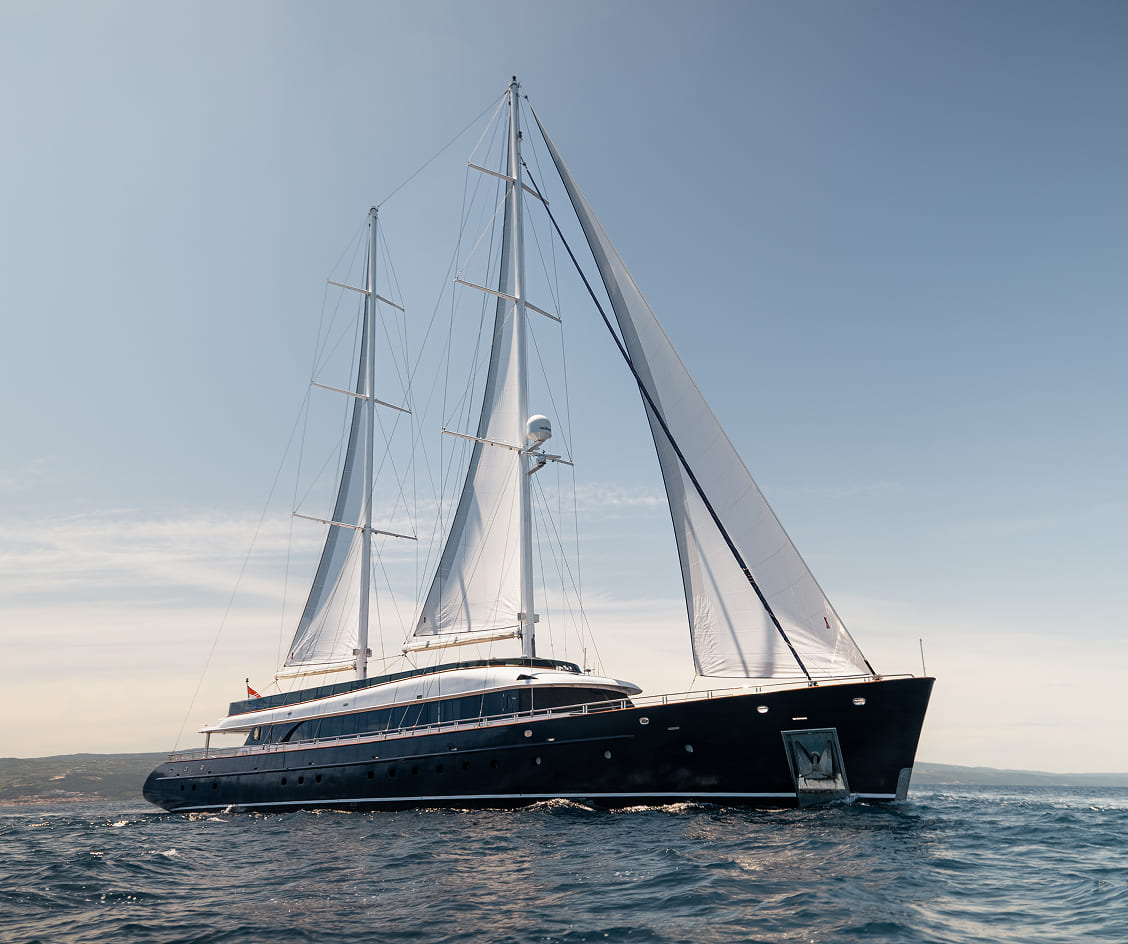 Large black sailing yacht with white sails on calm ocean waters under a clear sky.