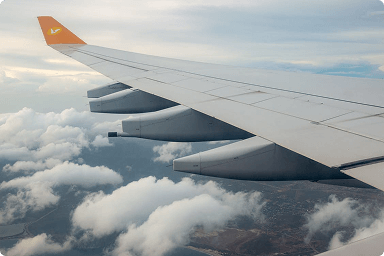 View of an airplane wing flying above clouds with some land visible below.