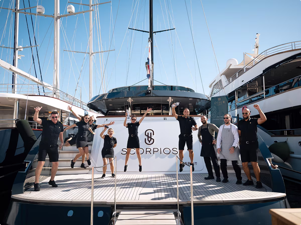 Group of people in black outfits posing energetically in front of a yacht named Reposado docked at a marina.