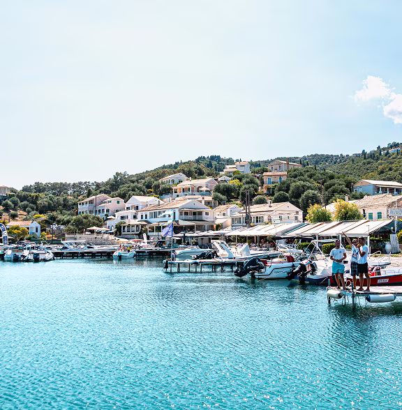 Coastal town with boats docked at piers and houses on a green hillside under a clear sky.