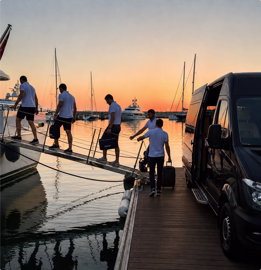 Crew members walking on a gangway to board a luxury yacht at sunset with a black van parked on a wooden dock.