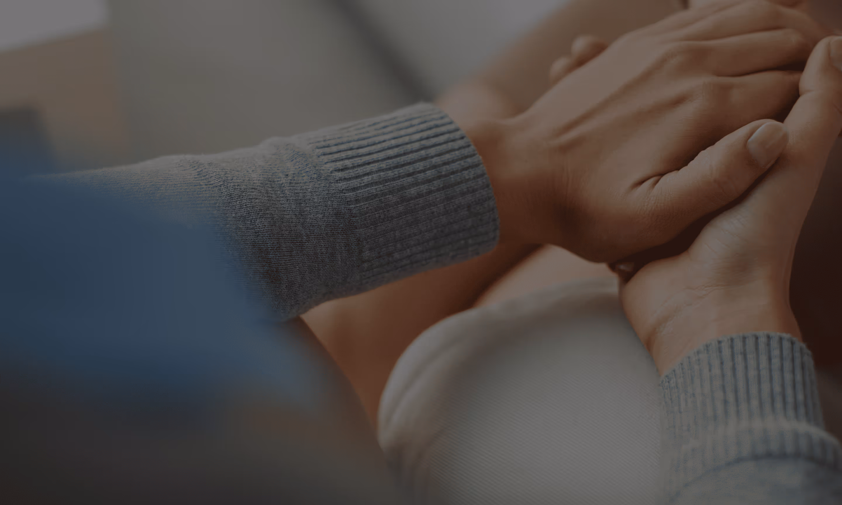 Close-up of two people holding hands, one wearing a gray ribbed sweater sleeve.