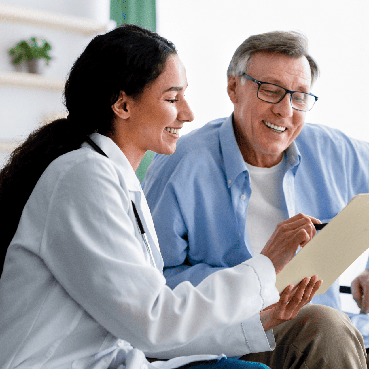 Smiling female doctor in white coat showing a clipboard to a happy elderly man wearing glasses and a blue shirt.