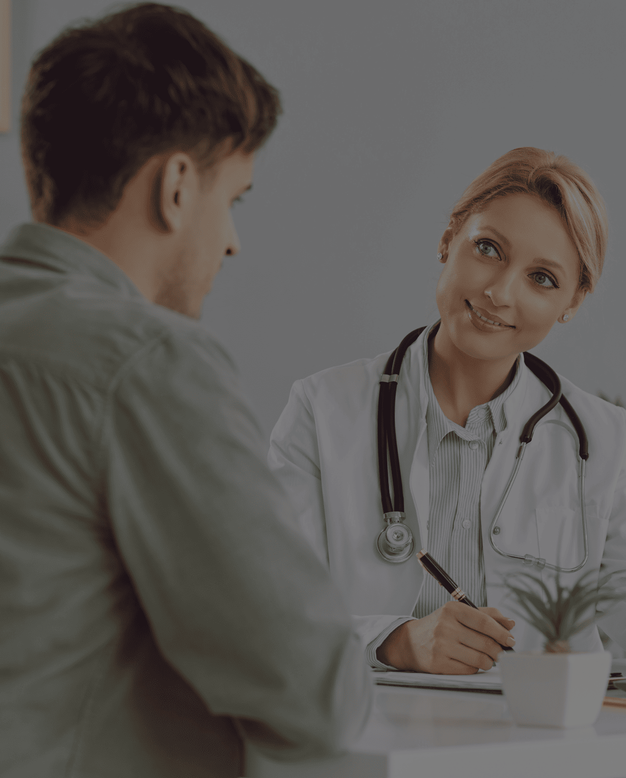 Female doctor with a stethoscope smiling and talking to a male patient during a consultation.