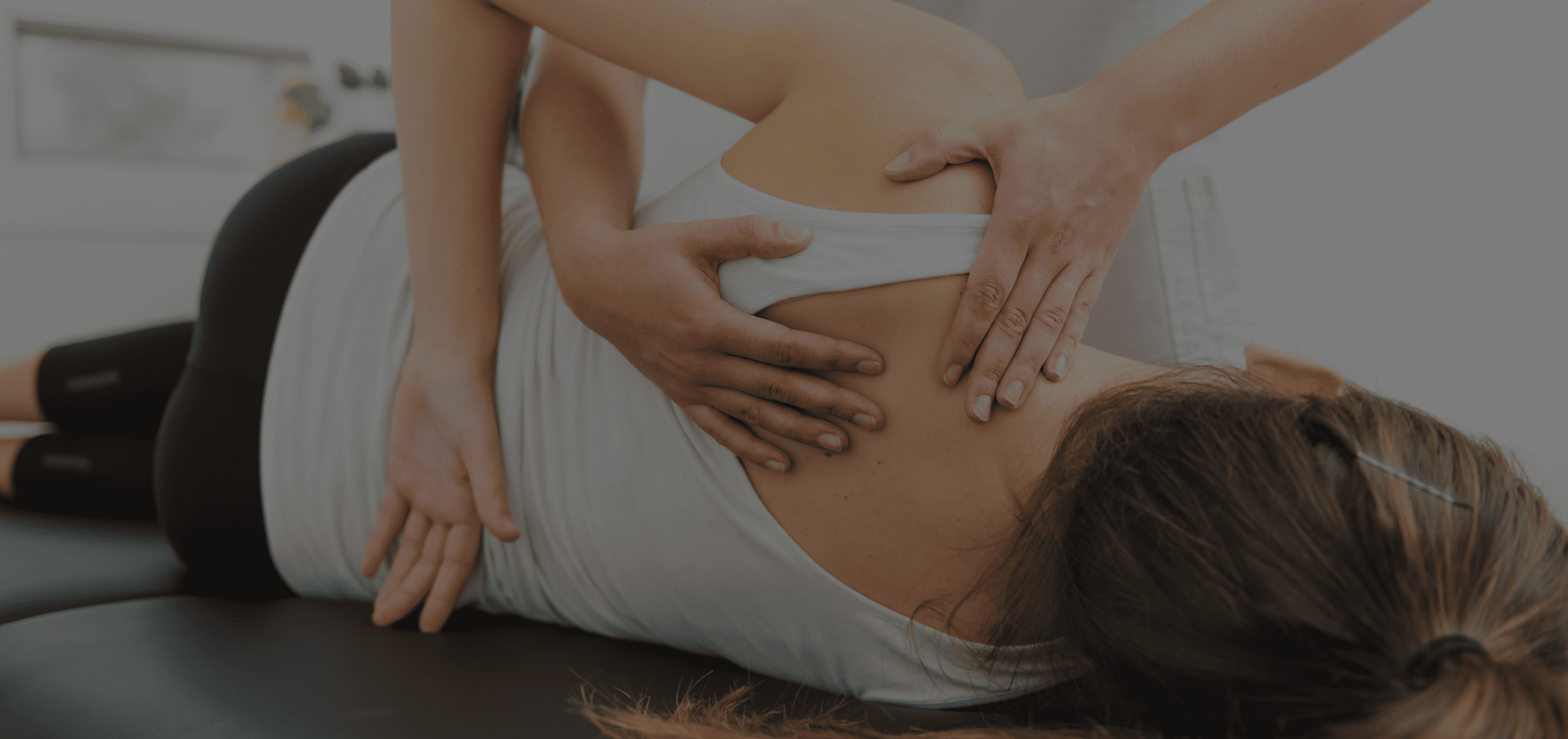 A chiropractor applying manual therapy by pressing on a woman's upper back while she lies face down on a treatment table.