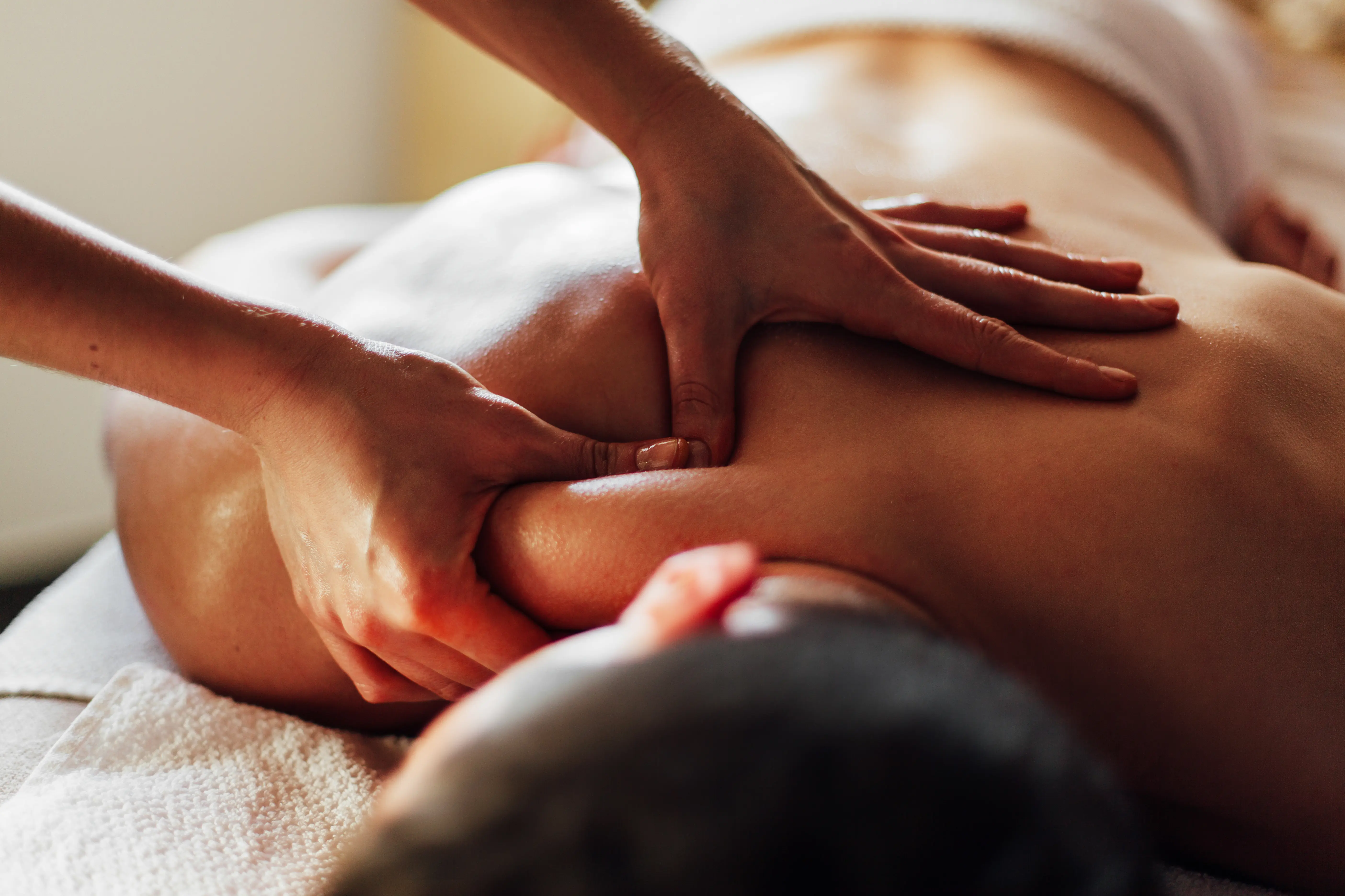 Close-up of a person receiving a back massage with hands pressing into shoulder muscles.