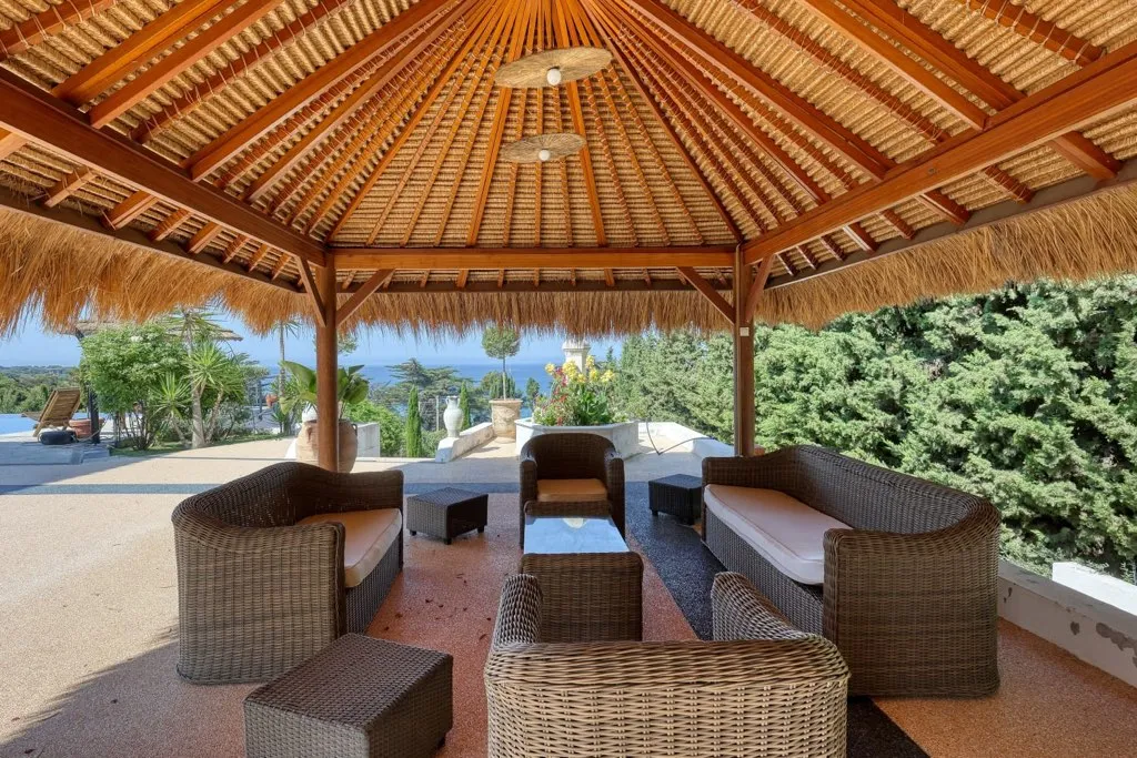 Grande paillotte située dans le jardin de la villa. On y retrouve des fauteuils, des canapés ainsi qu'une table basse.