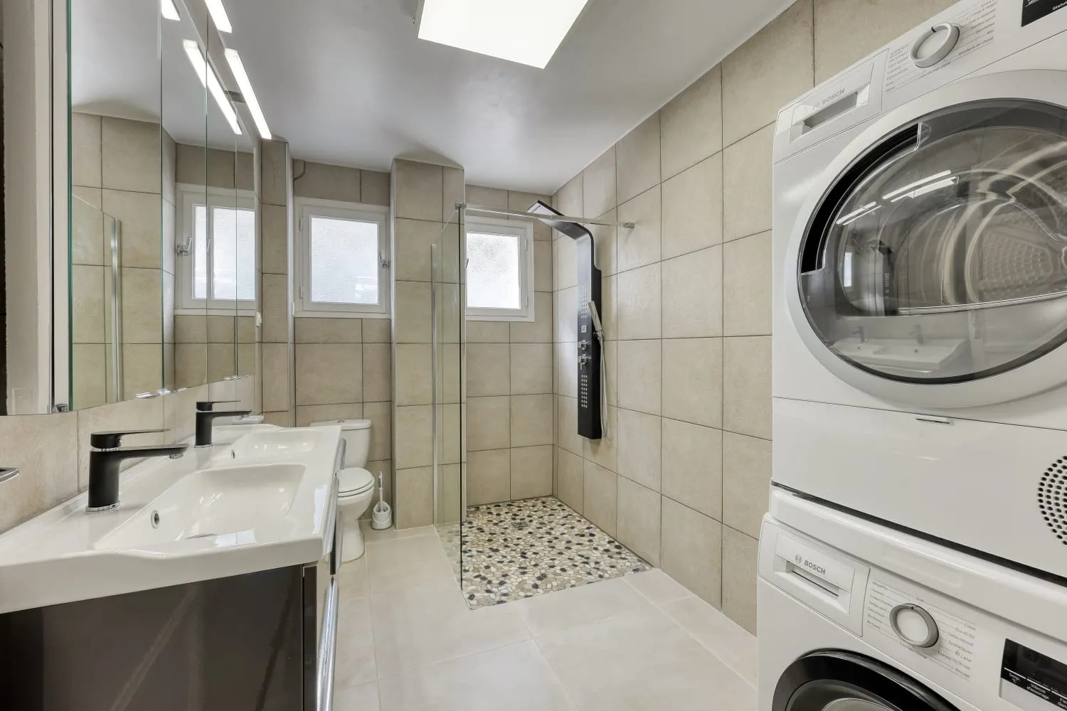 Salle de bain de la villa composée d'une douche, d'un wc, de double vasque, d'une machine à laver et d'un sèche linge.