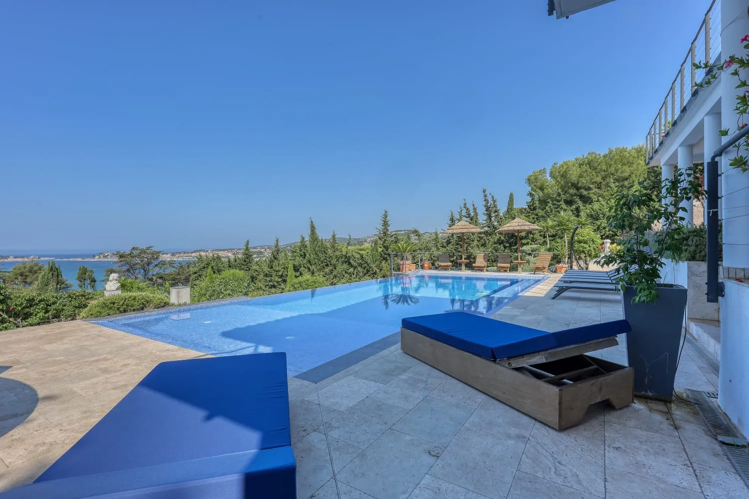Piscine à débordement avec de nombreux fauteuils et transat pour se reposer face à la mer.