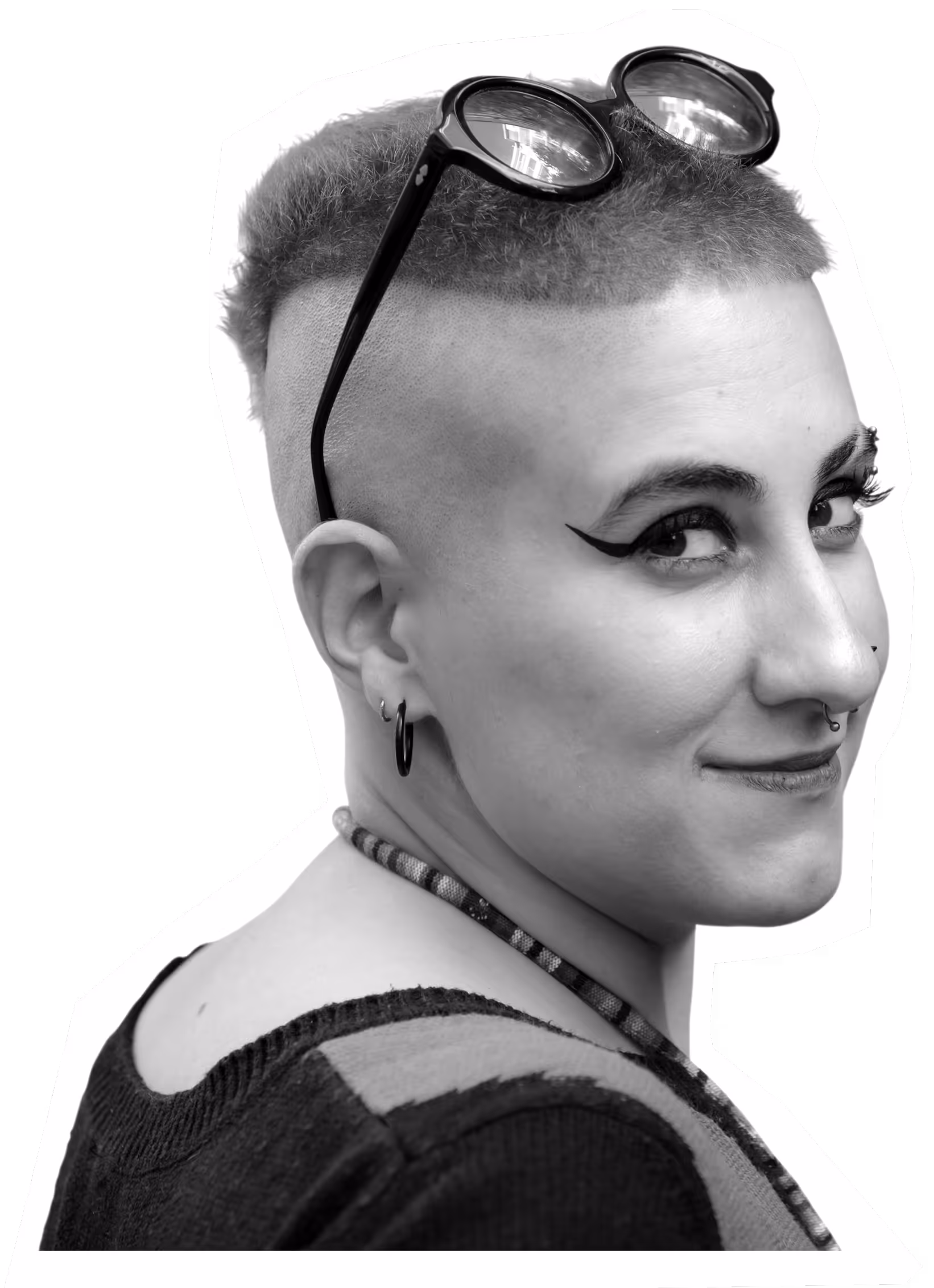 Smiling person with shaved head, goggles, and bold eye makeup