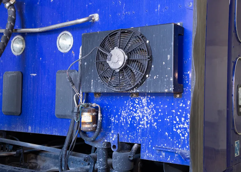 Auxiliary cooling fan mounted on a heavy-duty truck body with wiring and refrigerant filter visible.