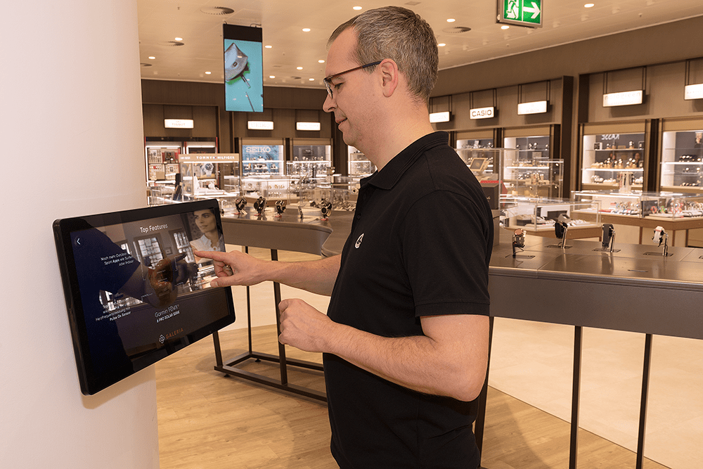 A man operates a touch display attached to a pillar in a department store.