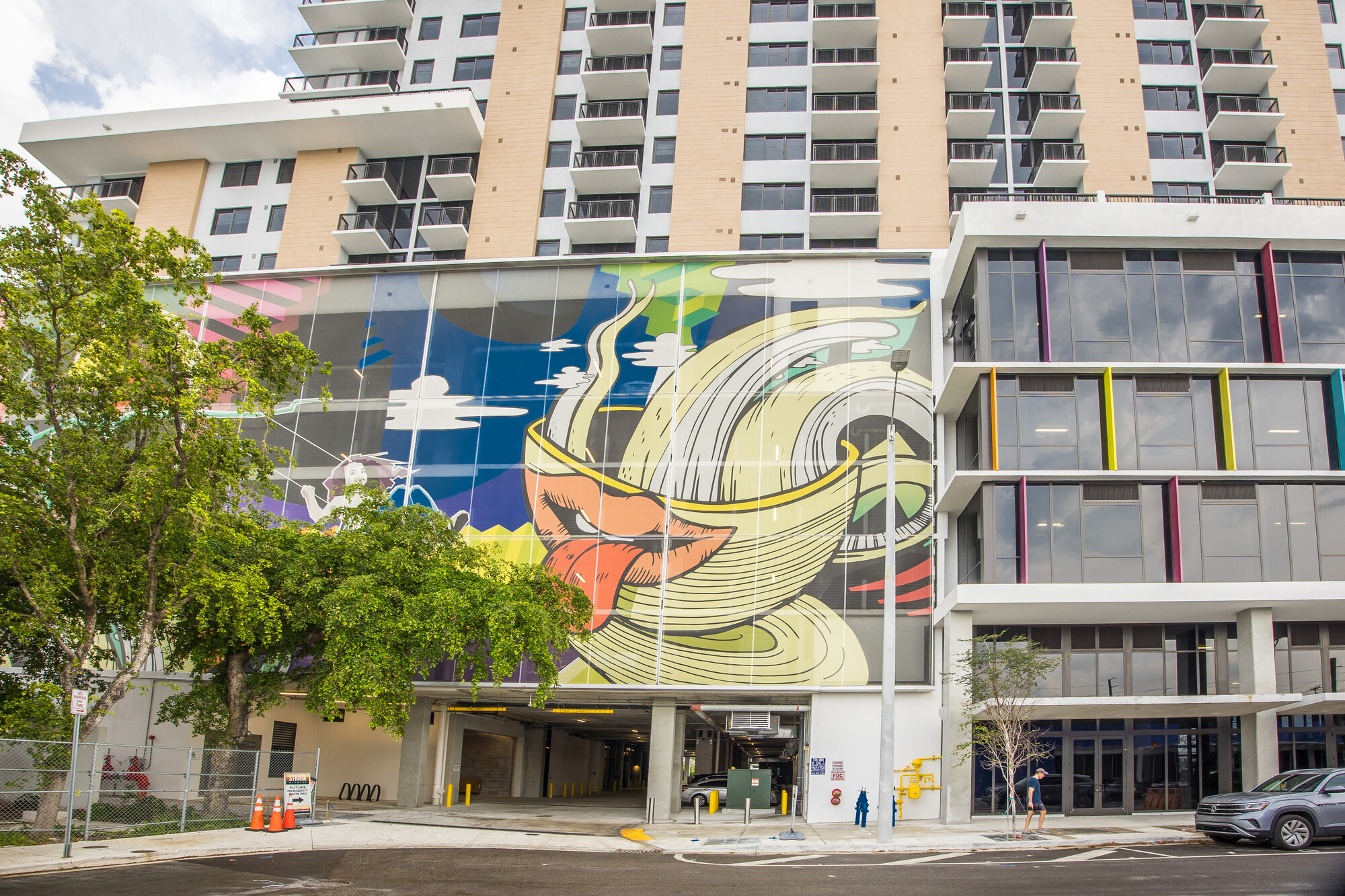 A graffiti-inspired tensile facade supported by a structural steel framework, peeking through some trees.