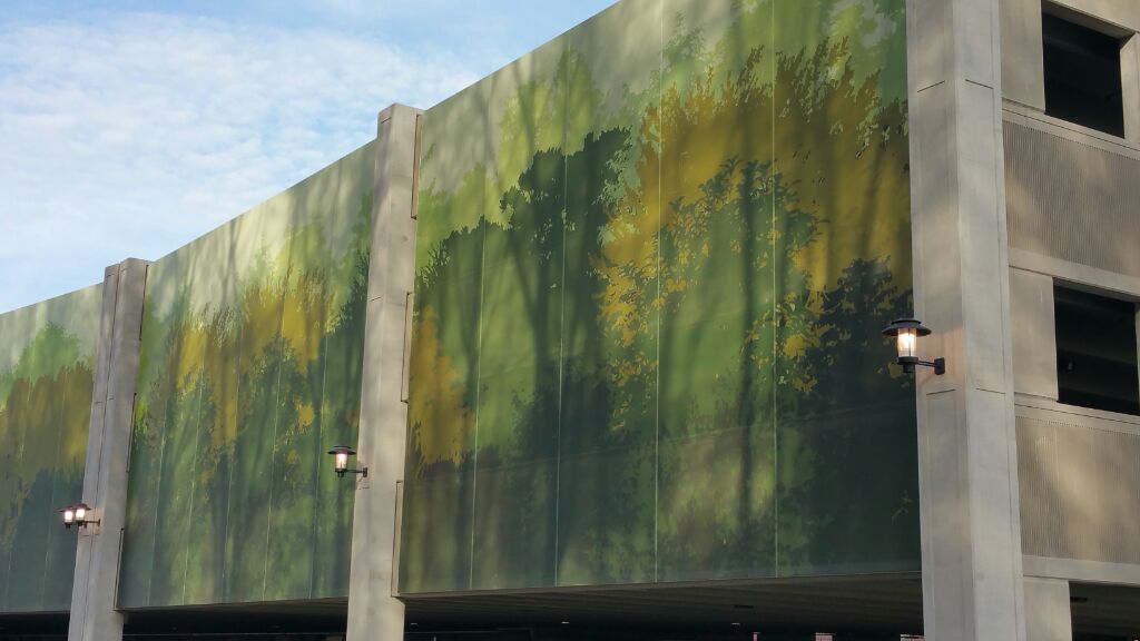 A green graphic parking garage facade that features  an abstract forrest scene.