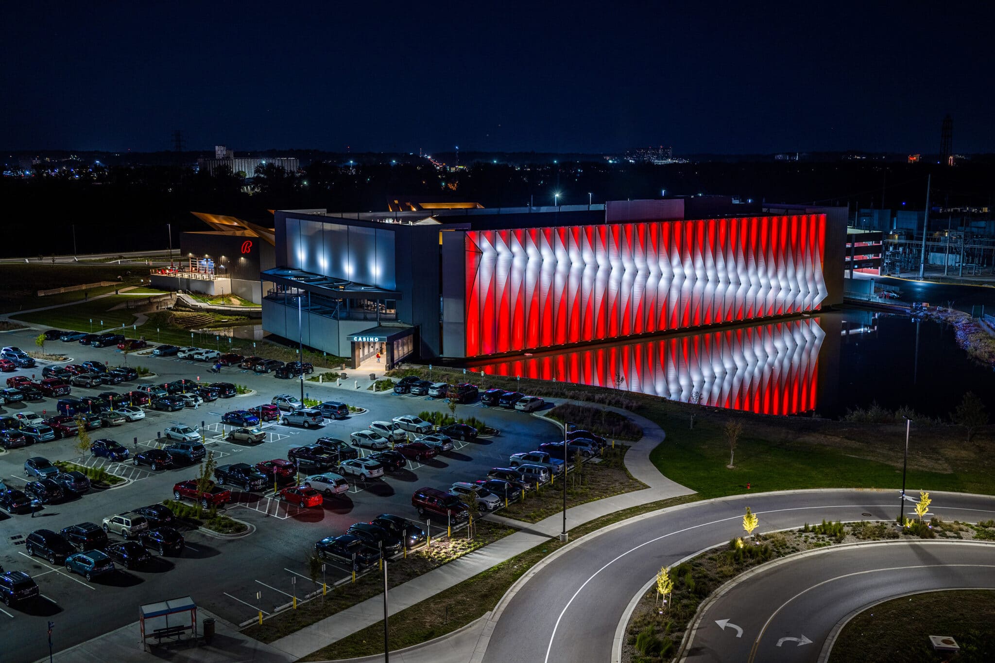 A lit up red and white finned facade on the side of a building that reflects off of the water below, creating a dual facade look.
