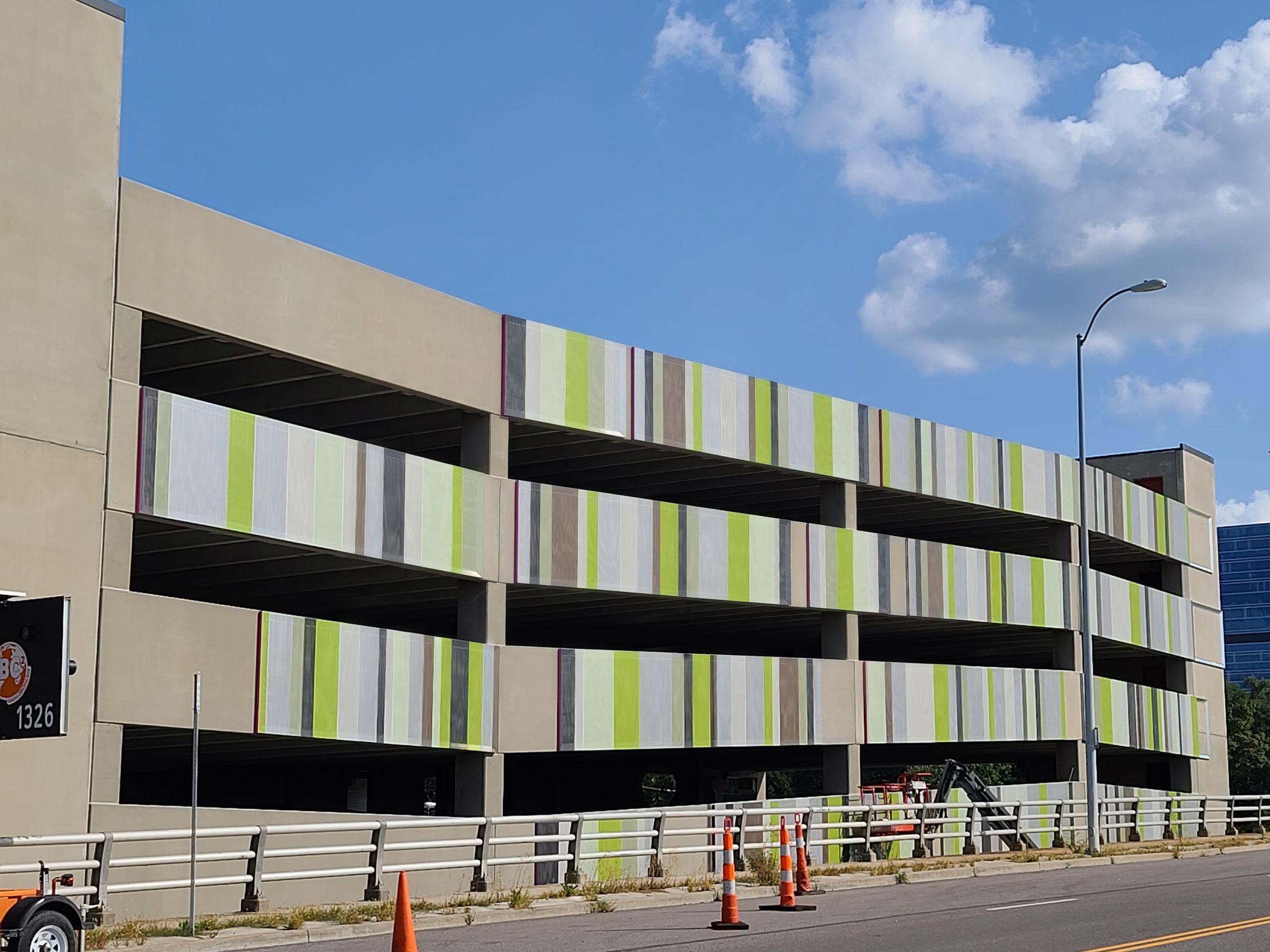 A lime green, white, grey, and black slotted facade sat on the concrete part of a parking garage.