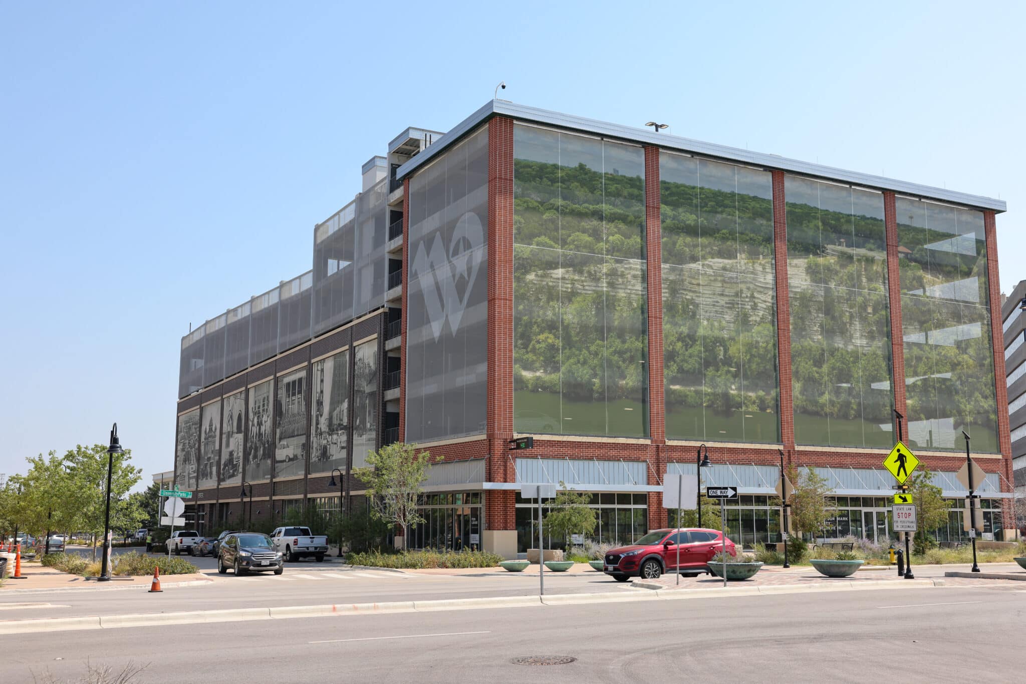 A view of a parking garage showing three different graphic facades, one featuring old images, another with a logo, and the third with printed forrest imagery.