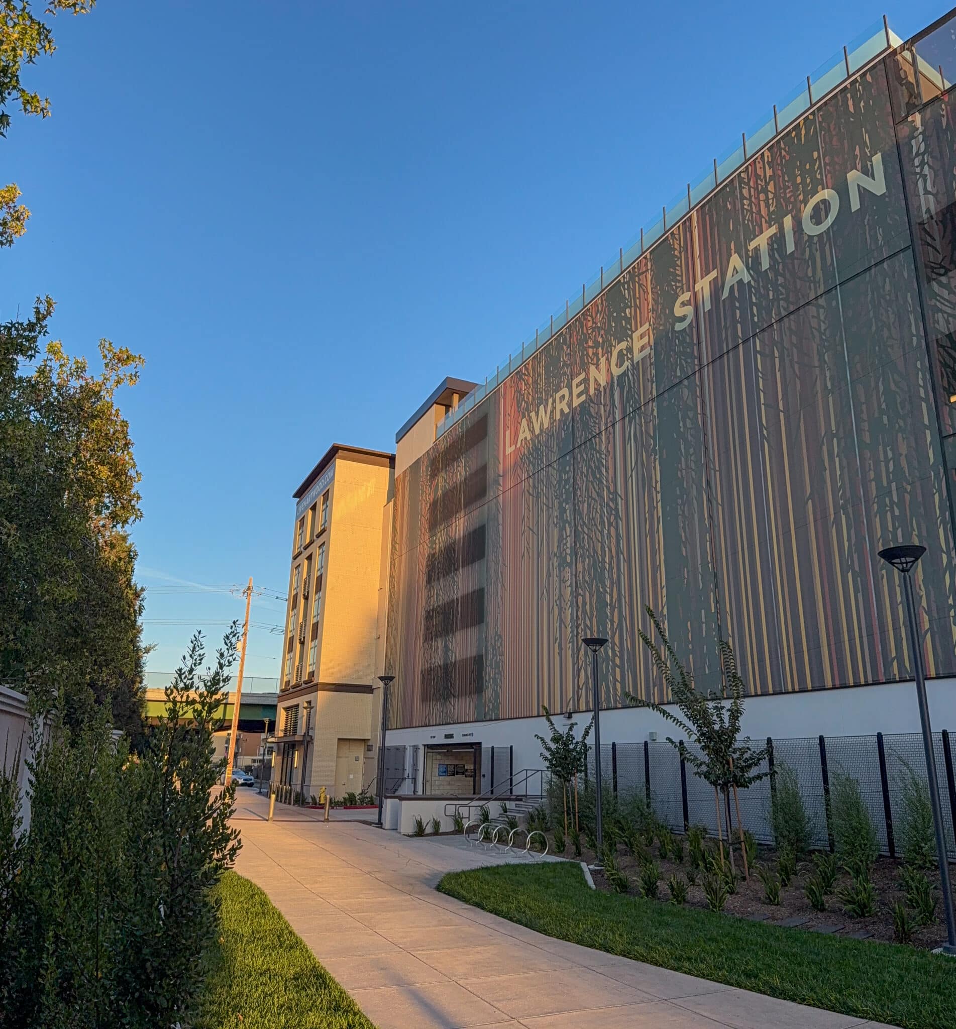 A photo of a parking garage facade with a colorful design that mimics the area's colorful life and the trees in front, allowing the facade to recede and to reduce the visual impact that a parking garage would typically have.