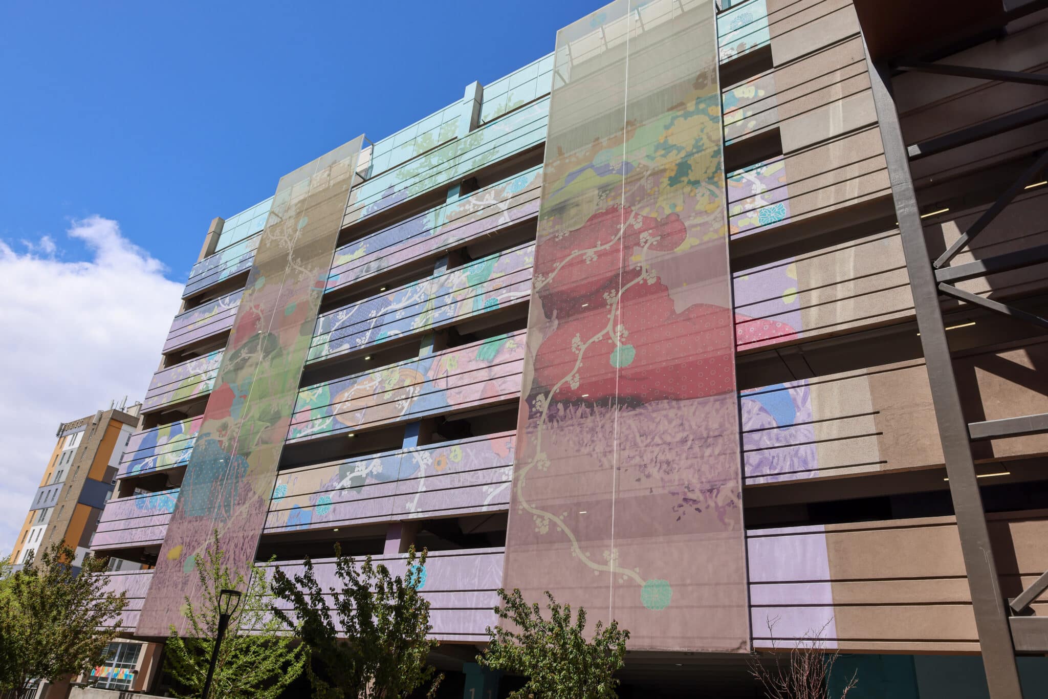 A colorful, layered mosaic facade sat on a parking garage. The facade is made from Ventilated PES and the artwork is from Daisy Patton.
