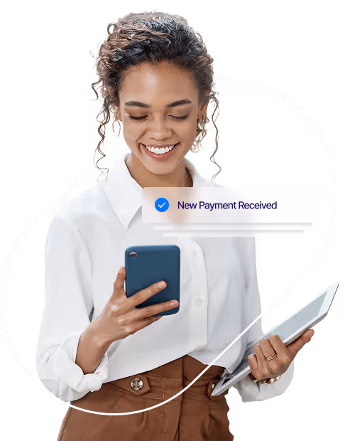 Smiling woman holding a phone and tablet, receiving a notification that says ‘New payment received.’
