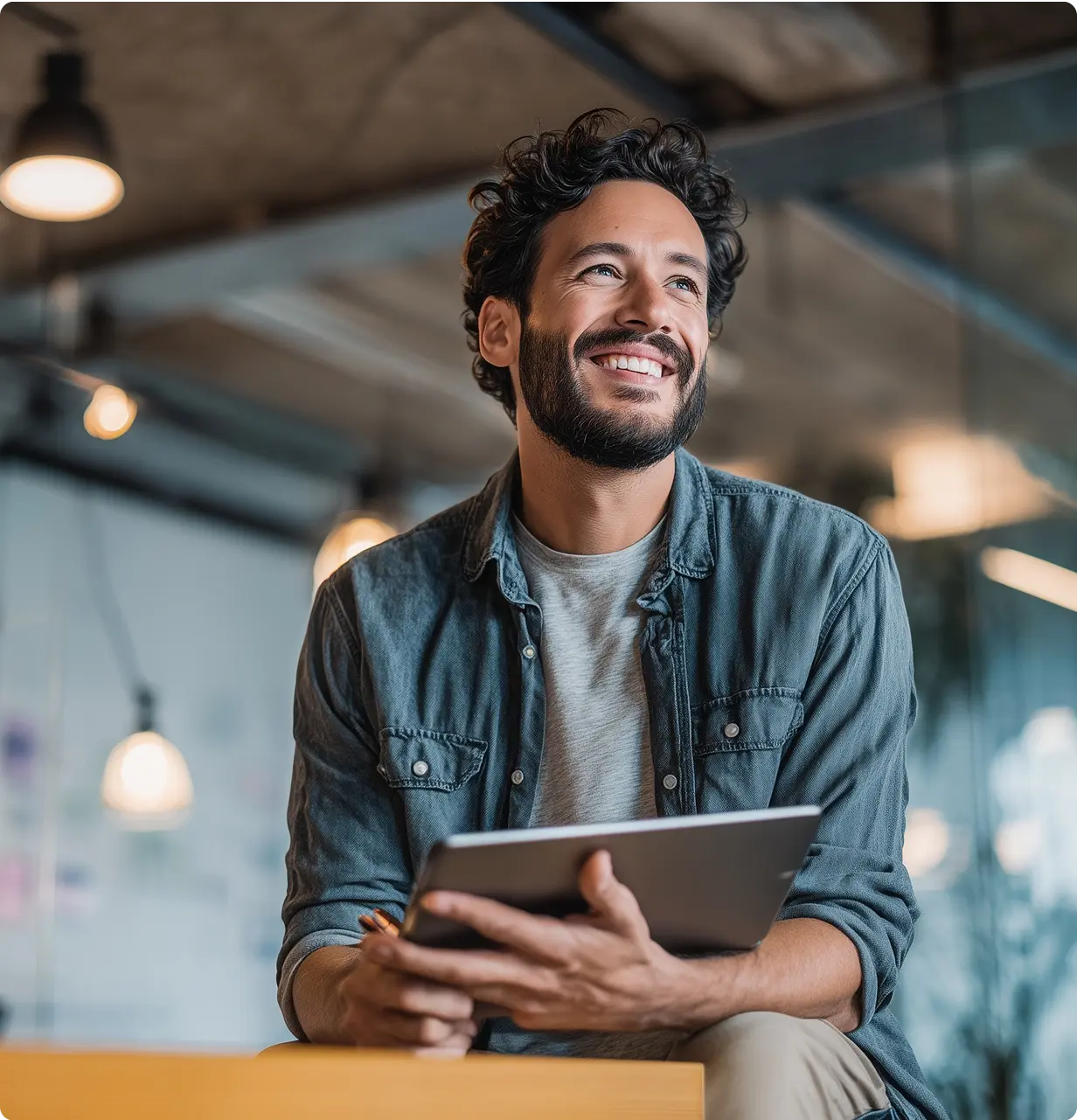 Smiling man holding a tablet in a modern office environment with warm lighting.