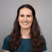 Portrait of a smiling woman with long brown hair wearing a teal top, against a neutral background.