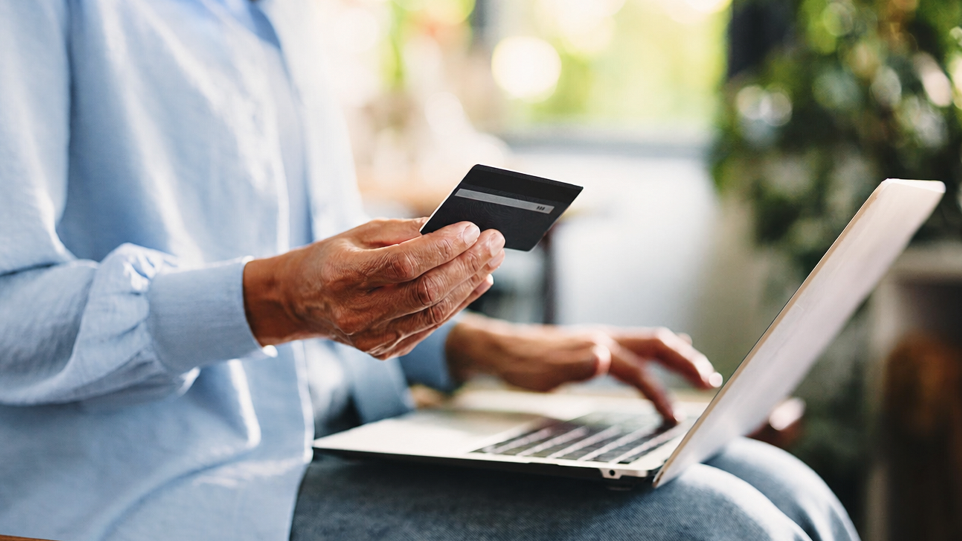 A person holding a bank card while making an online payment on a laptop.