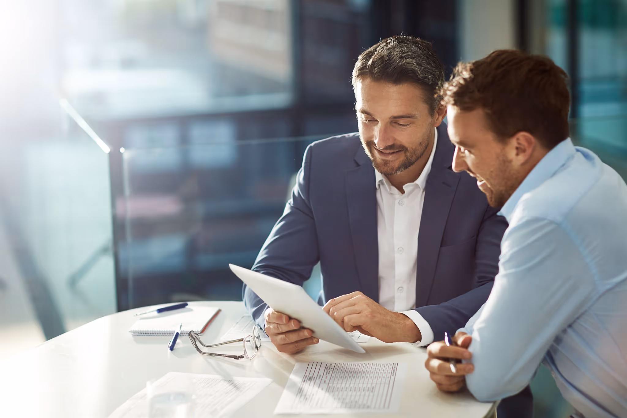 Two business professionals sitting at a modern office table reviewing a tablet together, symbolizing ELMA’s mission to empower organizations with practical, data-driven supply chain solutions that foster collaboration and measurable value.