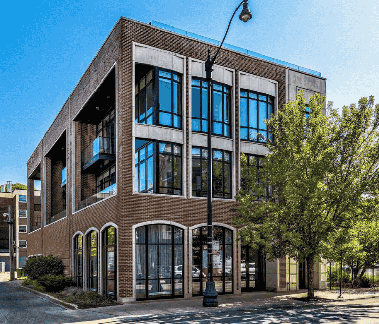Better Med Spa's modern two-story brick building with large windows, balconies, a street lamp, and a tree in front under a clear blue sky.
