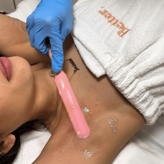 Person receiving a cosmetic armpit treatment with a pink device held by a gloved hand, lying on a white towel embroidered with 'Better'.