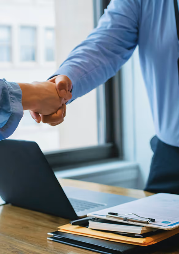 A handshake between two men at a desk over some documents.