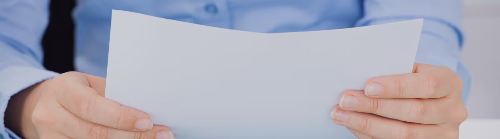 Person in blue shirt and black tie holding a blank white sheet of paper.