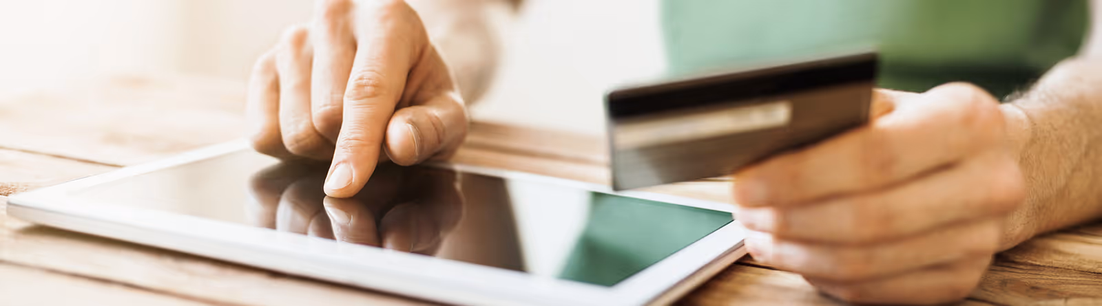Person holding a credit card and using a tablet on a wooden table.