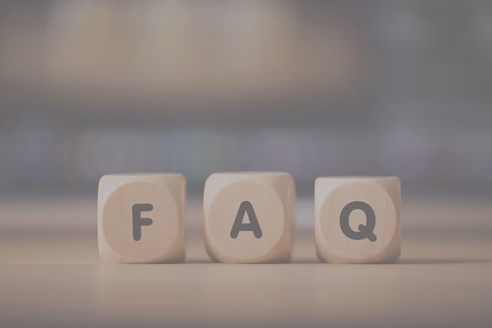Three wooden blocks on a surface arranged to spell 'FAQ'.