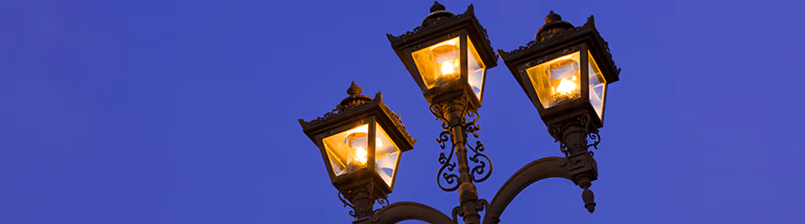 Three lit vintage street lamps against a clear twilight sky.