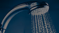 Close-up of water flowing from a modern showerhead against a dark background.